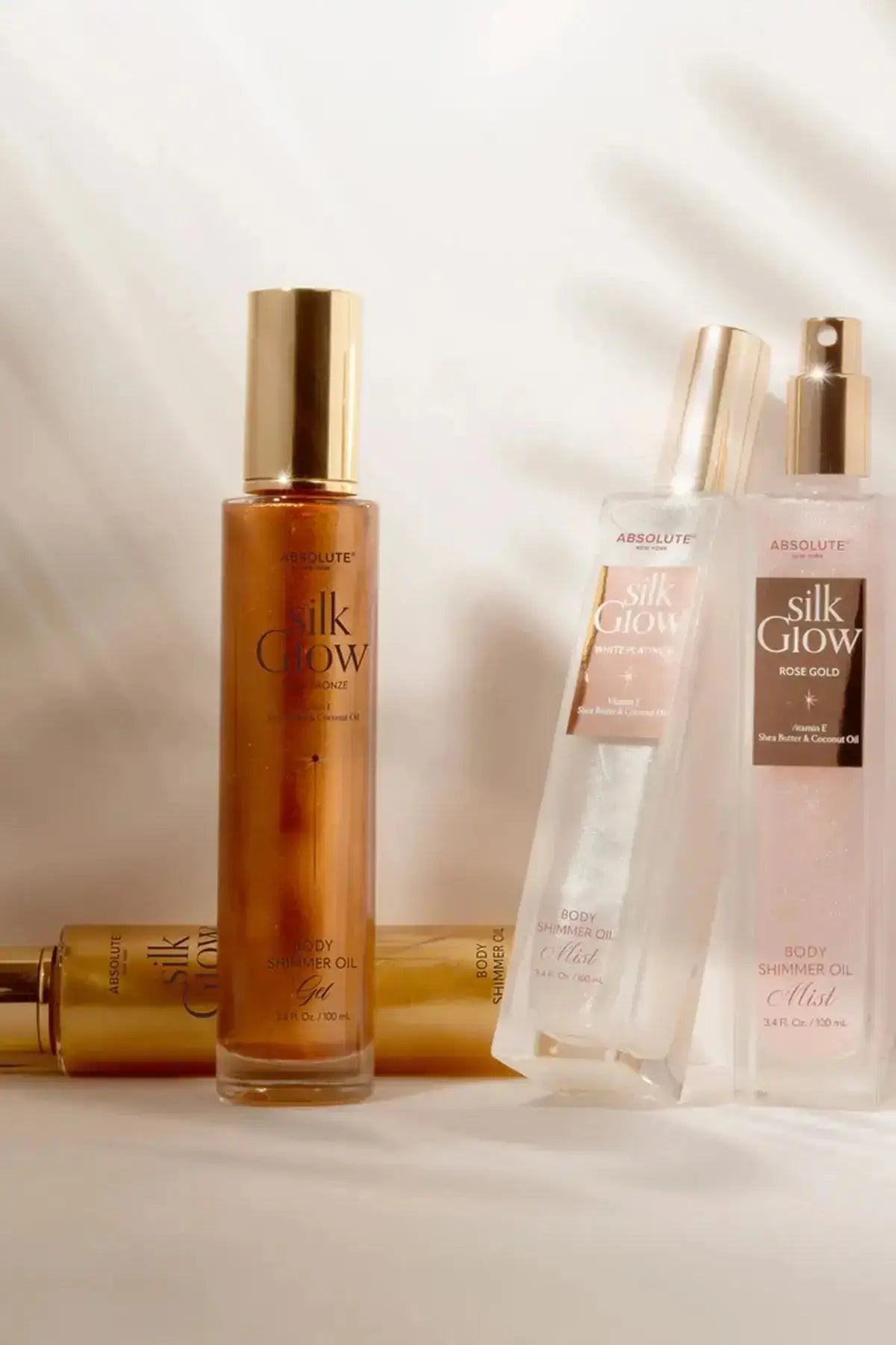 Absolute New York Silk Glow shimmer body collection on a tabletop with multiple bottles, featuring a Scented SHIMMER Body Mist in a warm, sunlit lifestyle scene.